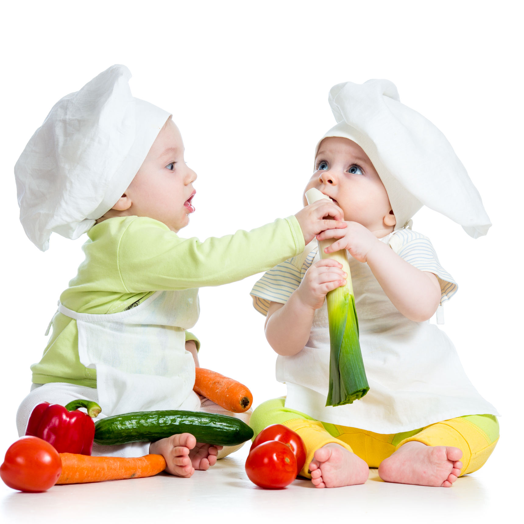 2 babyer der sidder med forskellige grøntsager og giver hinanden mad